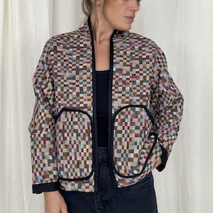 Può includere: Una giacca a quadri multicolore con bordi neri. La giacca ha un colletto e due tasche.