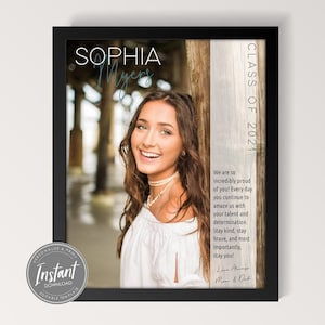 Puede incluir: Una foto de graduación enmarcada de Sophia Myers, clase de 2021. La foto está sobre un fondo de madera con un mensaje de felicitación y buenos deseos de sus padres.