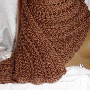 May include: A brown knitted scarf with a textured pattern. The scarf is draped over a white surface.