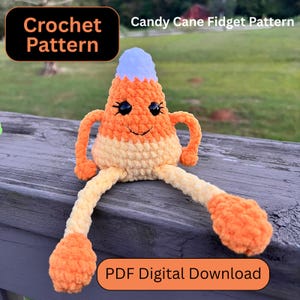 Puede incluir: Un juguete fidget de ganchillo con forma de caramelo de maíz, con brazos y piernas. El juguete es naranja, amarillo y azul claro, con una cara sonriente y ojos negros. El texto "Crochet Pattern" y "Candy Cane Fidget Pattern" son visibles.