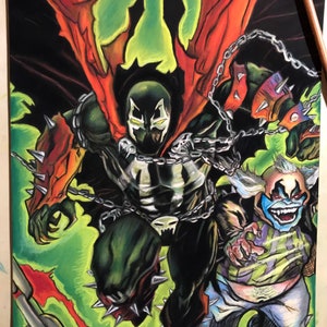 May include: A hand-drawn illustration of Spawn, a comic book character, with red and black wings, a black and green suit, and chains. He is fighting a smaller, green and blue character with a clown-like face. The background is green and red.