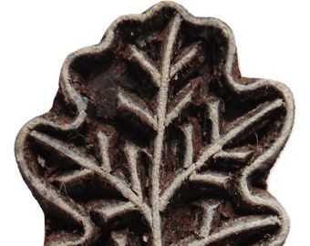 Puede incluir: Un bloque de madera tallado en forma de hoja de roble. La hoja está detallada con venas y tiene un color marrón oscuro.