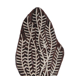 May include: A brown wooden block printing stamp with a white leaf design. The leaf design is made up of multiple thin lines that create a detailed pattern.
