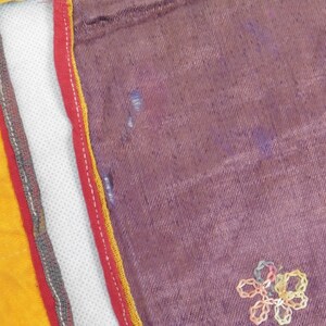 Puede incluir: Primer plano de una tela morada con un dise&ntilde;o de flor bordada en amarillo y rosa. La tela est&aacute; bordeada con ribetes rojos, amarillos y grises.
