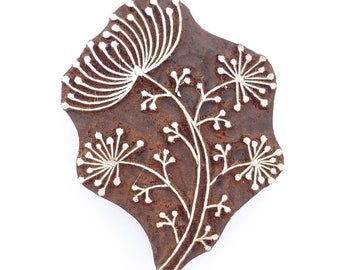 May include: A brown wooden block with a white floral design carved into it. The design features a central flower with several smaller flowers branching off from it.