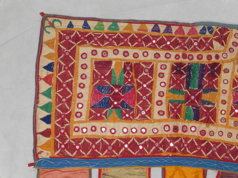 Puede incluir: Un tapiz de pared textil colorido con bordados intrincados y adornos de espejo. El dise&ntilde;o presenta patrones geom&eacute;tricos en tonos de rojo, naranja, amarillo, verde, azul y morado.