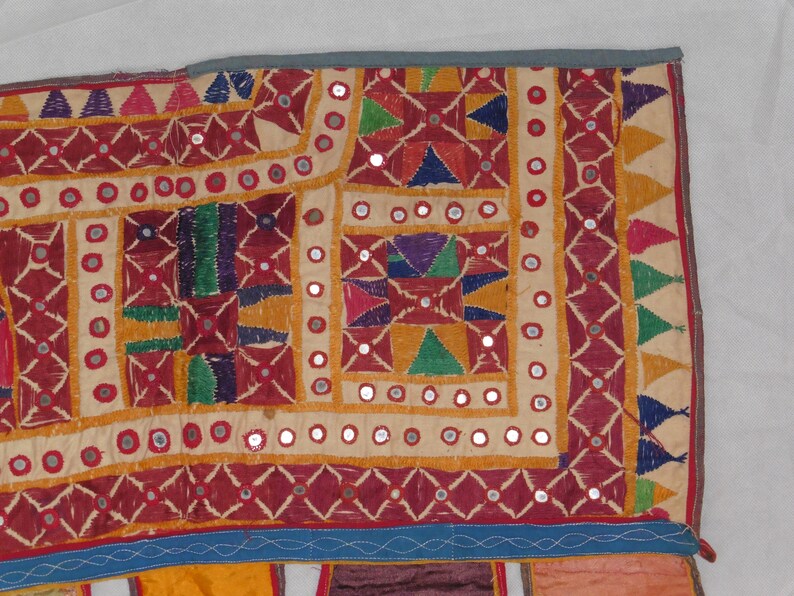 Puede incluir: Un tapiz de pared textil colorido con bordados intrincados y adornos de espejo. La tela es un mosaico de diferentes colores y patrones, incluyendo rojo, amarillo, verde, azul y morado. El tapiz est&aacute; decorado con peque&ntilde;os espejos redondos que est&aacute;n cosidos en la tela.