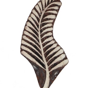 May include: A wooden block carving of a leaf, with a white design on a brown background. The leaf is a simple design with a central vein and parallel lines.
