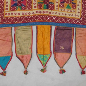 Puede incluir: Un tapiz de pared textil colorido con cinco borlas de tela. El tapiz est&aacute; hecho de varias telas en tonos de rojo, naranja, amarillo, verde, azul y morado. Las borlas est&aacute;n hechas de tela roja, azul, verde y amarilla.
