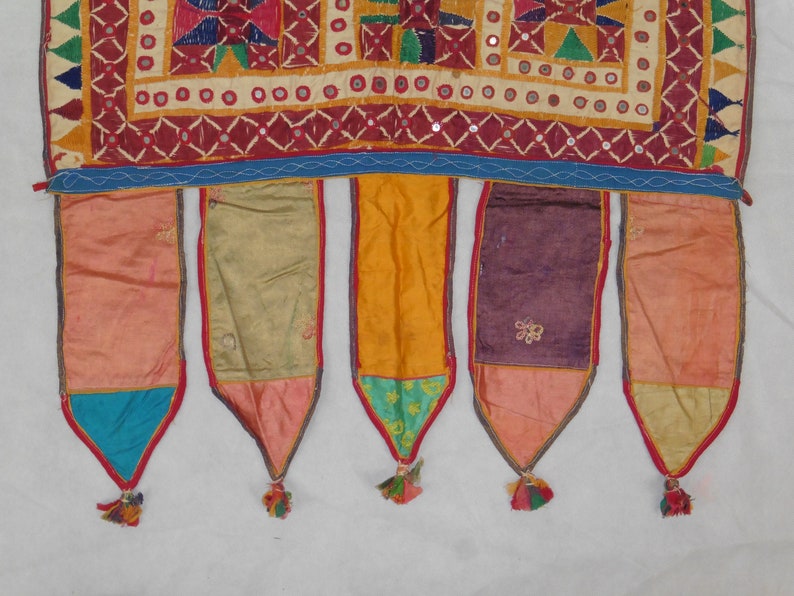 Puede incluir: Un tapiz de pared textil colorido con cinco borlas de tela. El tapiz est&aacute; hecho de varias telas en tonos de rojo, naranja, amarillo, verde, azul y morado. Las borlas est&aacute;n hechas de tela roja, azul, verde y amarilla.