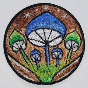 Peut inclure: Patch brodé représentant un champignon bleu et blanc sur fond brun. Le patch a un design fantaisiste avec des champignons verts et blancs entourant le champignon principal.