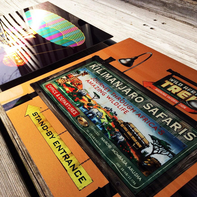 May include: A collection of vintage travel signs and posters. The main sign reads "Kilimanjaro Safaris, Journey Through Africa's Amazing Wildlife." Other signs include "Stand-By Entrance" and "Wild Africa Trek." The signs are orange, green, and yellow.