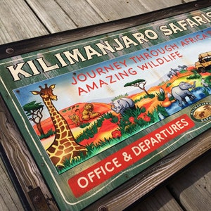May include: A vintage-style sign for Kilimanjaro Safaris, featuring a giraffe, lions, elephants, and rhinos in an African landscape. The sign reads "Journey Through Africa's Amazing Wildlife" and "Office & Departures."