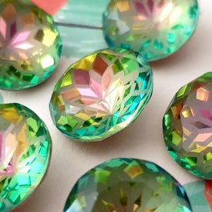 May include: Close-up of several iridescent, faceted oval beads. The beads have a mosaic-like appearance with a mix of green, yellow, pink, and blue colours. The light reflects off the facets, creating a sparkling effect. These beads are suitable for jewellery making.