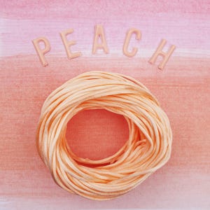 May include: A circular bundle of peach-coloured satin ribbon sits on a pink and peach watercolour background. The word "PEACH" is spelled out in peach-coloured letters above the ribbon.