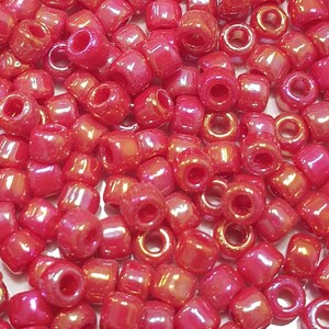 May include: A close-up image of a large quantity of small, red, iridescent glass beads. The beads are round and have a hole in the centre. They are ideal for jewellery making or other craft projects.