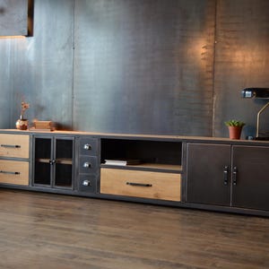 Peut inclure: Meuble TV de style industriel avec une structure métallique et des éléments en bois. Il comprend des tiroirs, des placards et des étagères ouvertes. La palette de couleurs comprend des nuances de gris, de marron et de bois naturel. Une petite lampe et une plante sont posées dessus.