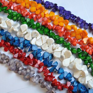 May include: A collection of colorful, handcrafted gemstone beads in a variety of colors, including red, orange, yellow, green, blue, and purple. The beads are arranged in rows, showcasing their unique shapes and textures. Ideal for jewelry making.