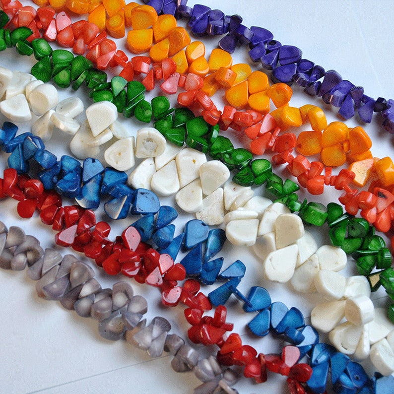 May include: A collection of colorful, handcrafted gemstone beads in a variety of colors, including red, orange, yellow, green, blue, and purple. The beads are arranged in rows, showcasing their unique shapes and textures. Ideal for jewelry making.