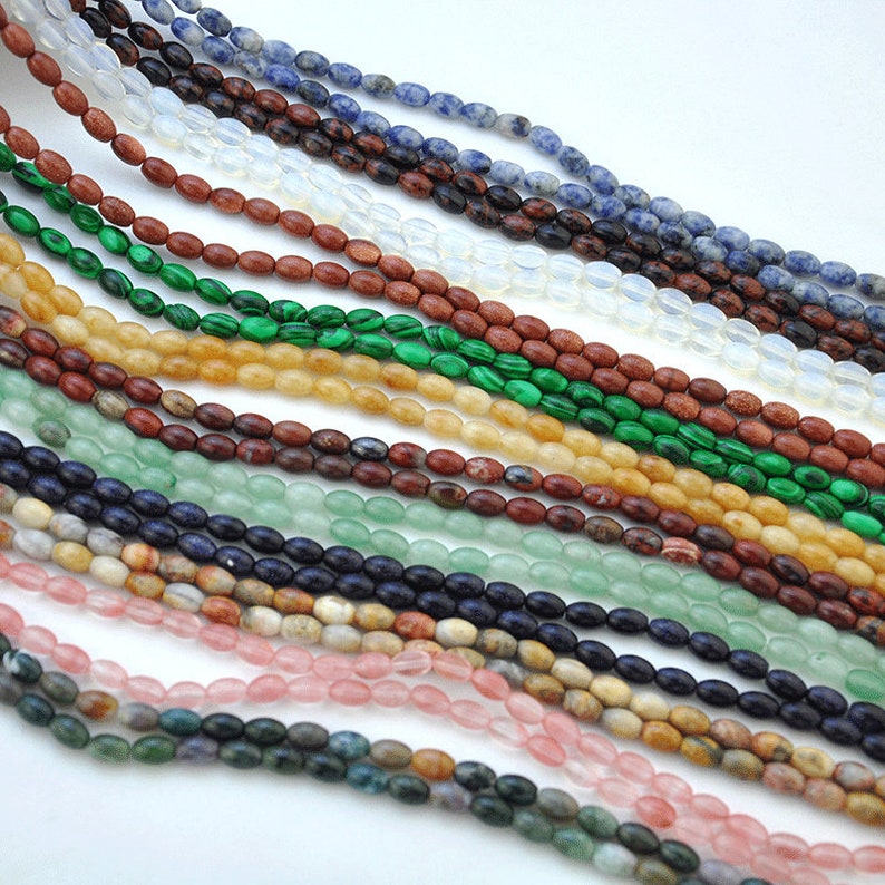 Pu&ograve; includere: Assortimento di perline di pietre preziose di forma ovale in vari colori, tra cui verde, blu, marrone e rosa. Le perline sono disposte in file, creando una visualizzazione colorata e visivamente accattivante.