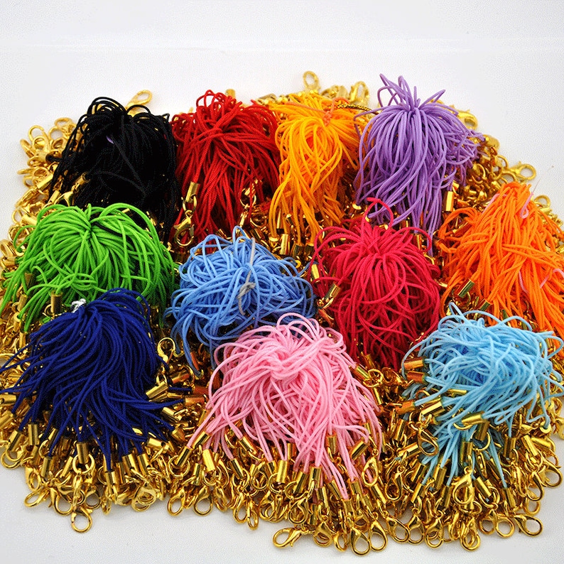 May include: A large assortment of colorful elastic cords with gold metal clasps. The cords are bundled together in a variety of colors, including black, red, orange, purple, green, blue, pink, and light blue.
