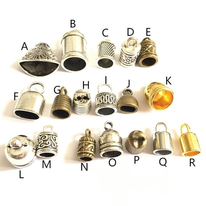 May include: Assortment of 18 silver and gold metal bell charms with various designs. The charms are labeled with letters A through R.