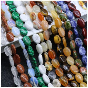 Peut inclure: Assortiment de perles de pierres précieuses de forme ovale dans différentes couleurs, notamment le vert, le bleu, le marron, l'orange et le blanc. Les perles sont enfilées sur un fil transparent et sont prêtes pour la fabrication de bijoux.