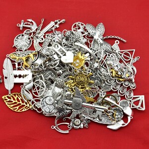 May include: A large pile of silver and gold metal charms, including a key, a dragonfly, a feather, a heart, a star, a crescent moon, and a leaf. The charms are on a red background.
