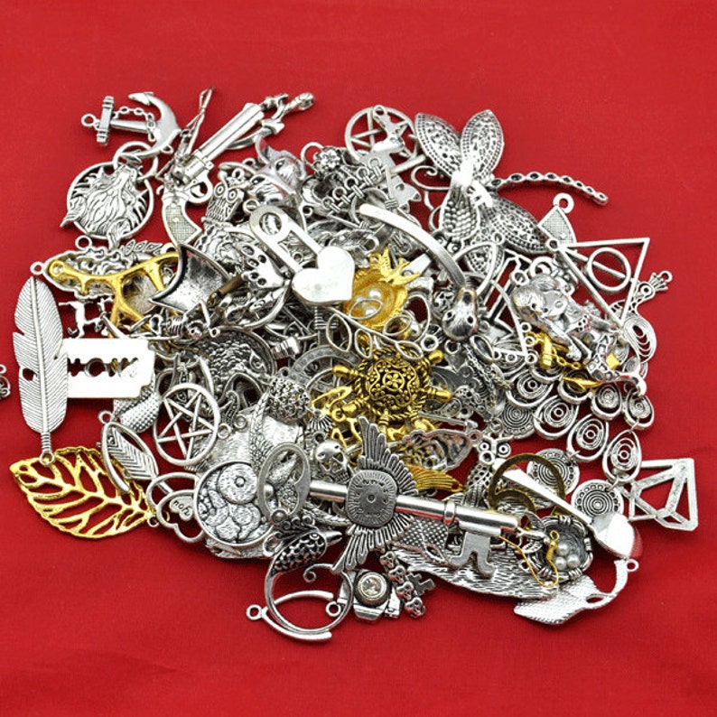 May include: A large pile of silver and gold metal charms, including a key, a dragonfly, a feather, a heart, a star, a crescent moon, and a leaf. The charms are on a red background.