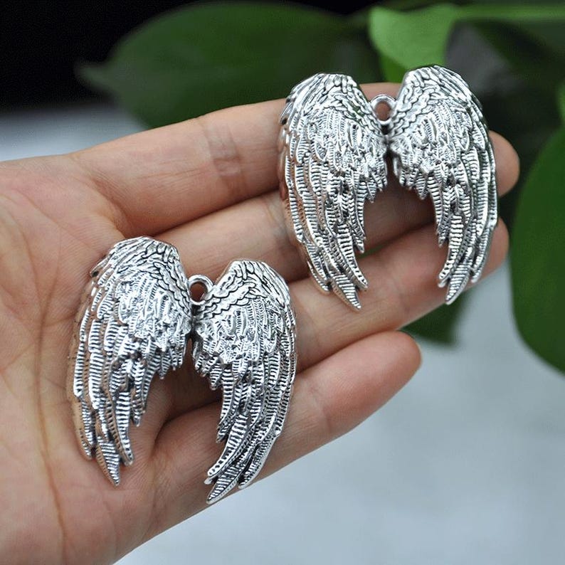 May include: Two pairs of silver-colored angel wing charms. Each wing is intricately detailed with feather patterns. The charms are designed with a loop at the top for easy attachment to jewelry or other crafts.