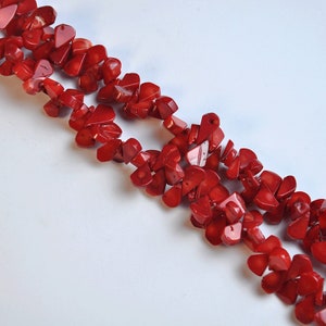 May include: Two strands of vibrant red coral chip beads are displayed against a white background. The coral pieces are irregularly shaped, creating a textured and natural look. The beads are likely used for jewelry making.