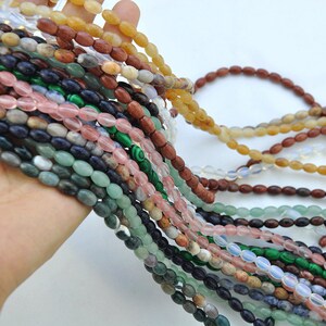 Pu&ograve; includere: Assortimento di perline di pietre preziose di forma ovale in vari colori, tra cui verde, rosa, marrone, blu e bianco. Le perline sono infilate su una corda e sono disposte in uno schema a strati.