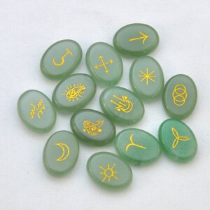 May include: Set of 12 green oval-shaped stones with gold symbols. The symbols include a crescent moon, a sun, a star, a cross, a hand with a flame, a circle with a dot in the center, a circle with three rings, a circle with a spiral, a circle with a crescent moon, a circle with a star, a circle with an arrow, and a circle with a wave.