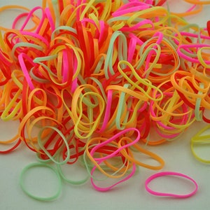 Pu&ograve; includere: Un grande mucchio di elastici colorati in rosa, arancio, giallo e verde.