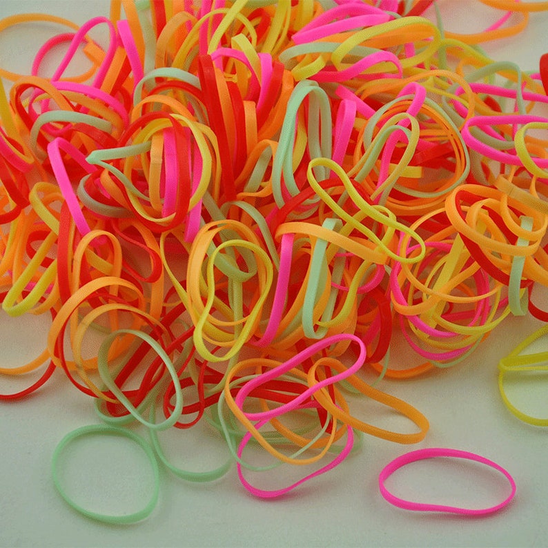 Pu&ograve; includere: Un grande mucchio di elastici colorati in rosa, arancio, giallo e verde.