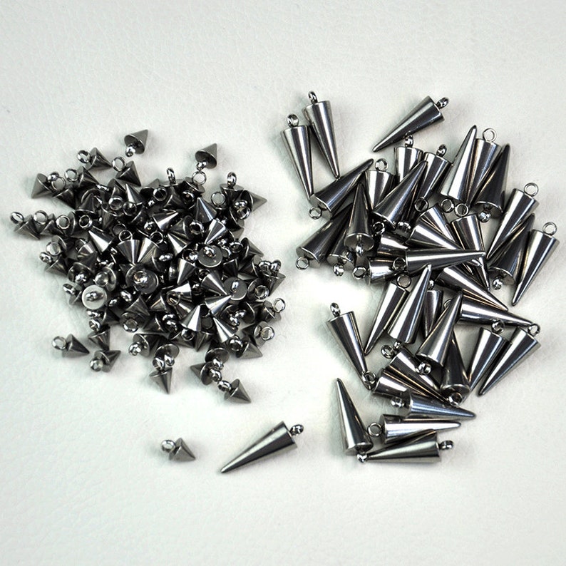 Puede incluir: Dos pilas de tachuelas de metal plateado en forma de pir&aacute;mide con un bucle en la parte superior. Las tachuelas est&aacute;n dispuestas en un patr&oacute;n aleatorio.