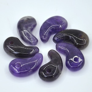 May include: Seven polished amethyst stones shaped like a crescent moon with a hole drilled through the top. The stones are a deep purple color with some lighter areas.
