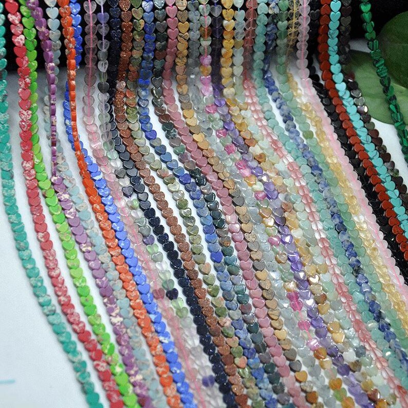 Puede incluir: Una colecci&oacute;n de cuentas en forma de coraz&oacute;n en varios colores, incluyendo rojo, verde, azul y rosa. Las cuentas est&aacute;n ensartadas, creando m&uacute;ltiples hebras. Las cuentas parecen ser de piedra o vidrio, y son adecuadas para la fabricaci&oacute;n de joyas.