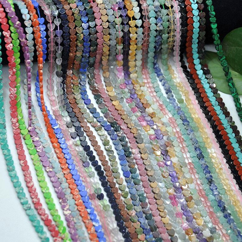 Puede incluir: Una colecci&oacute;n de cuentas en forma de coraz&oacute;n en varios colores, incluyendo verde, naranja, morado y azul. Las cuentas est&aacute;n ensartadas, creando un efecto en cascada. Las cuentas son probablemente para hacer joyas.