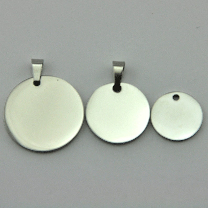 May include: Three silver metal round blank tags with a hole at the top. The tags are different sizes.