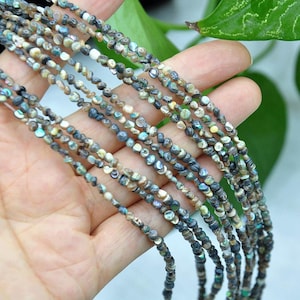 May include: Multiple strands of small, irregular, iridescent abalone shell beads. The beads feature a mix of dark gray, blue, green, and cream tones with a natural, polished luster. Each strand consists of tiny, rounded shell fragments strung together.