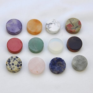 May include: Twelve round, polished, smooth, flat, gemstone coasters in various colours, including purple, orange, white, red, green, light blue, grey, black, brown, pink, and speckled black and white.