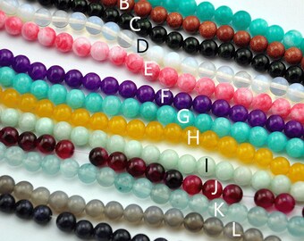 Könnte beinhalten: Nahaufnahme einer Auswahl an Perlen in verschiedenen Farben und Materialien, darunter Rot, Rosa, Lila, Türkis, Gelb, Grün und Grau. Die Perlen sind in Reihen angeordnet, wobei jede Reihe eine andere Art von Perle darstellt.
