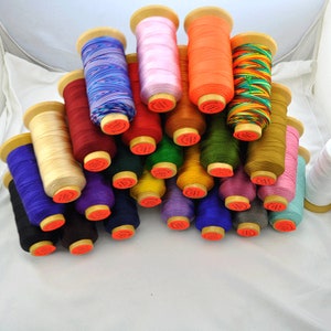 May include: A collection of colorful thread spools. The spools are made of wood and hold various colors of thread, including blue, pink, orange, green, and yellow. The threads are tightly wound and ready for use in sewing or crafting projects.