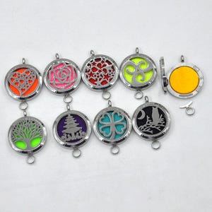 Puede incluir: Una colección de colgantes de aromaterapia plateados con varios diseños, incluyendo un corazón, una rosa y un árbol. Cada colgante tiene una almohadilla de fieltro de color en el interior. Los colgantes son redondos y tienen un pequeño lazo para una cadena.