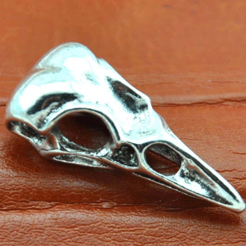 May include: Silver bird skull pendant charm. The skull is detailed with a beak and eye sockets.