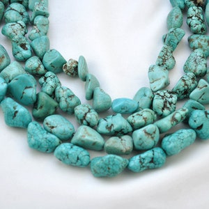 May include: A strand of turquoise gemstone beads, featuring a light blue colour with brown veining. The beads are irregularly shaped and have a smooth, polished finish.