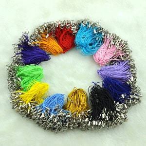 May include: Assortment of colorful string keychains with silver metal clasps. The keychains are arranged in a circle on a white surface.