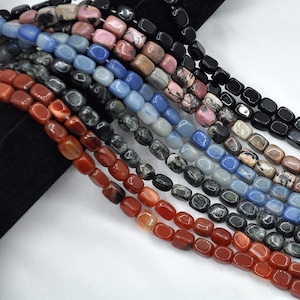May include: A strand of colorful gemstone beads, including red, blue, black, and pink, in a rectangular shape. The beads are strung on a cord and are ready to be used for jewelry making.
