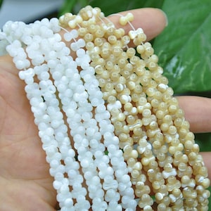 May include: Multiple strands of small, polished beads shaped like tiny bones or hourglasses, strung together. The beads are arranged in two distinct color groups, with one set being a bright, opaque white and the other a warm, translucent beige.
